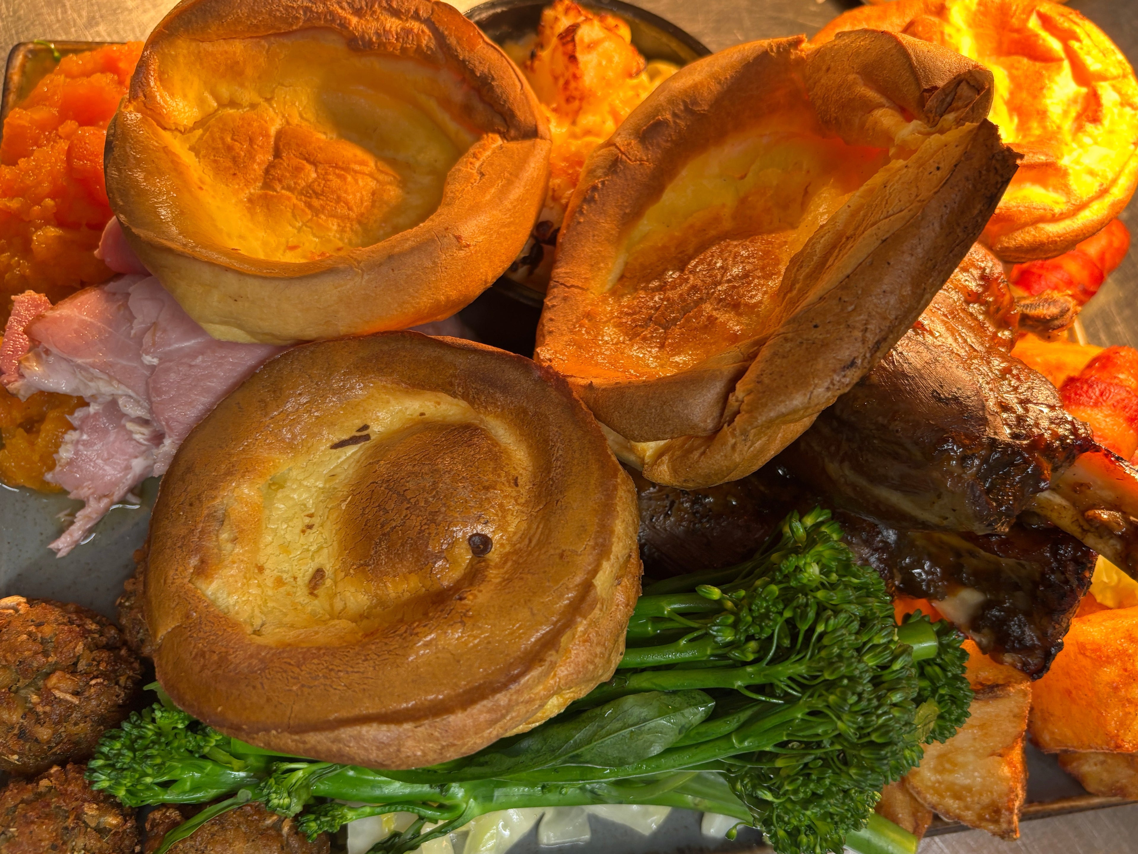 Plated dish with roasted vegetables, meat, and Yorkshire puddings on a wooden surface.